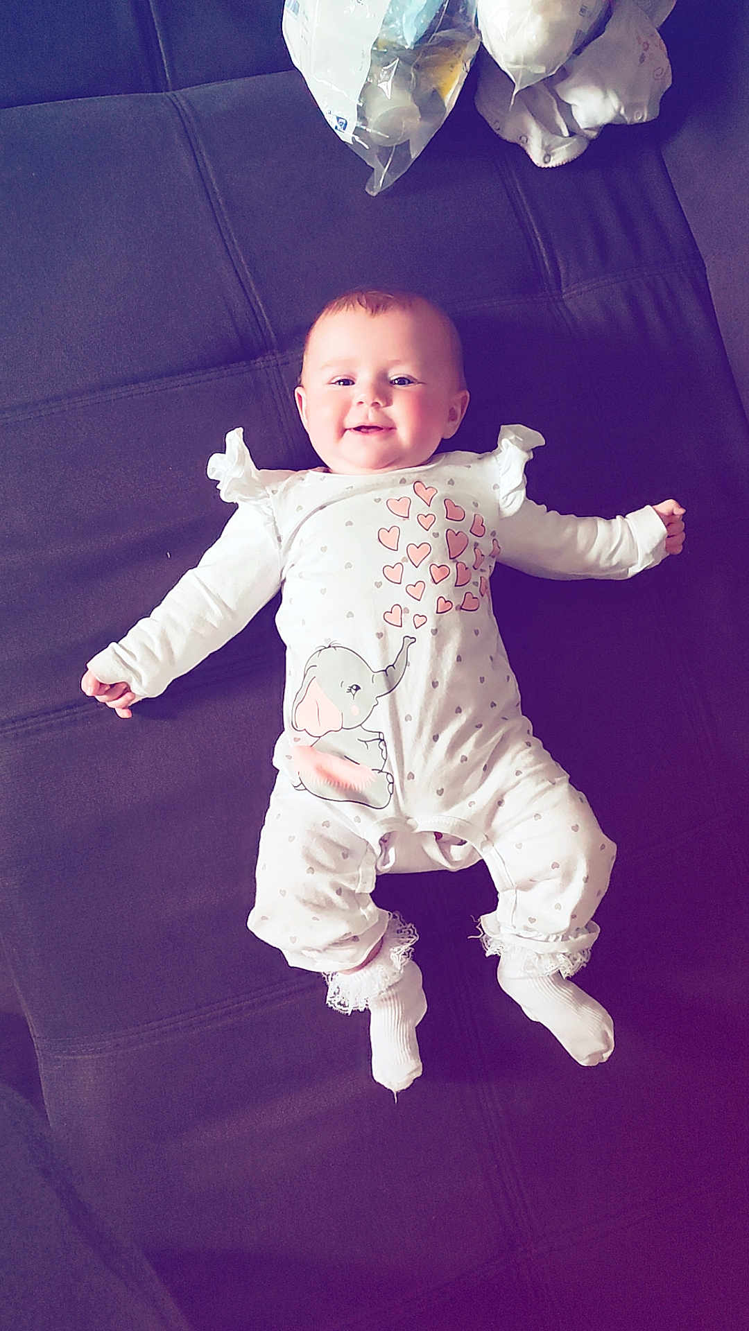 Laïa participe au concours pour gagner de l'argent avec cette photo : baby, infant, smiling, onesie, elephant, hearts, white_clothing, socks, lace, couch, furniture, indoor, child, person, happy, cute, resting, lying_down, soft_lighting, cozy