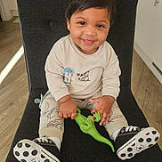 Syron is registered to the contest to win money with this photo: black_chair, cabinet, child, clothing, cute, dinosaur_toy, flooring, hand, happy, indoor, kitchen, pacifier_clip, person, polka_dots, portrait, sitting, smiling, sneakers, toddler, toy