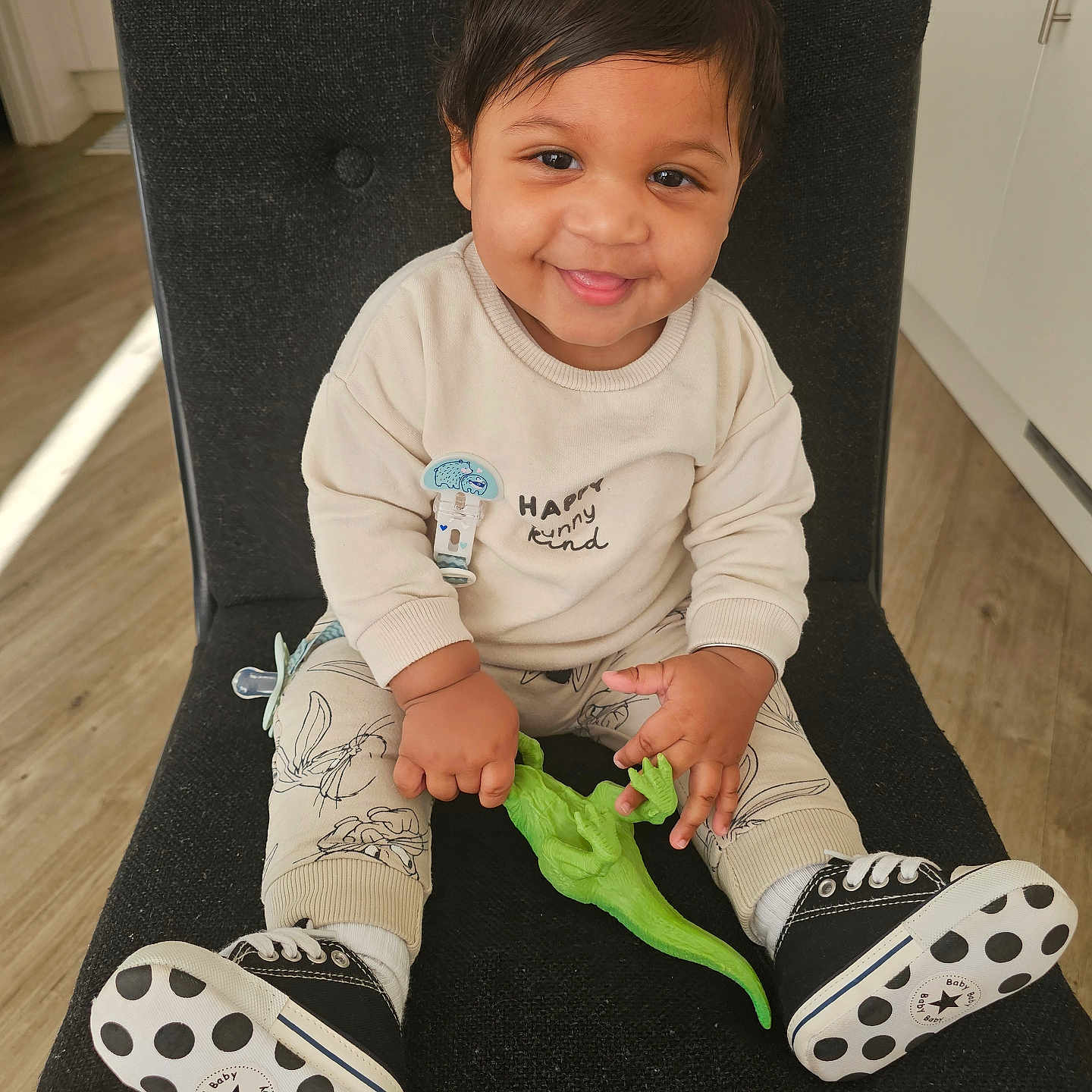 Syron is registered to the contest to win money with this photo: black_chair, cabinet, child, clothing, cute, dinosaur_toy, flooring, hand, happy, indoor, kitchen, pacifier_clip, person, polka_dots, portrait, sitting, smiling, sneakers, toddler, toy