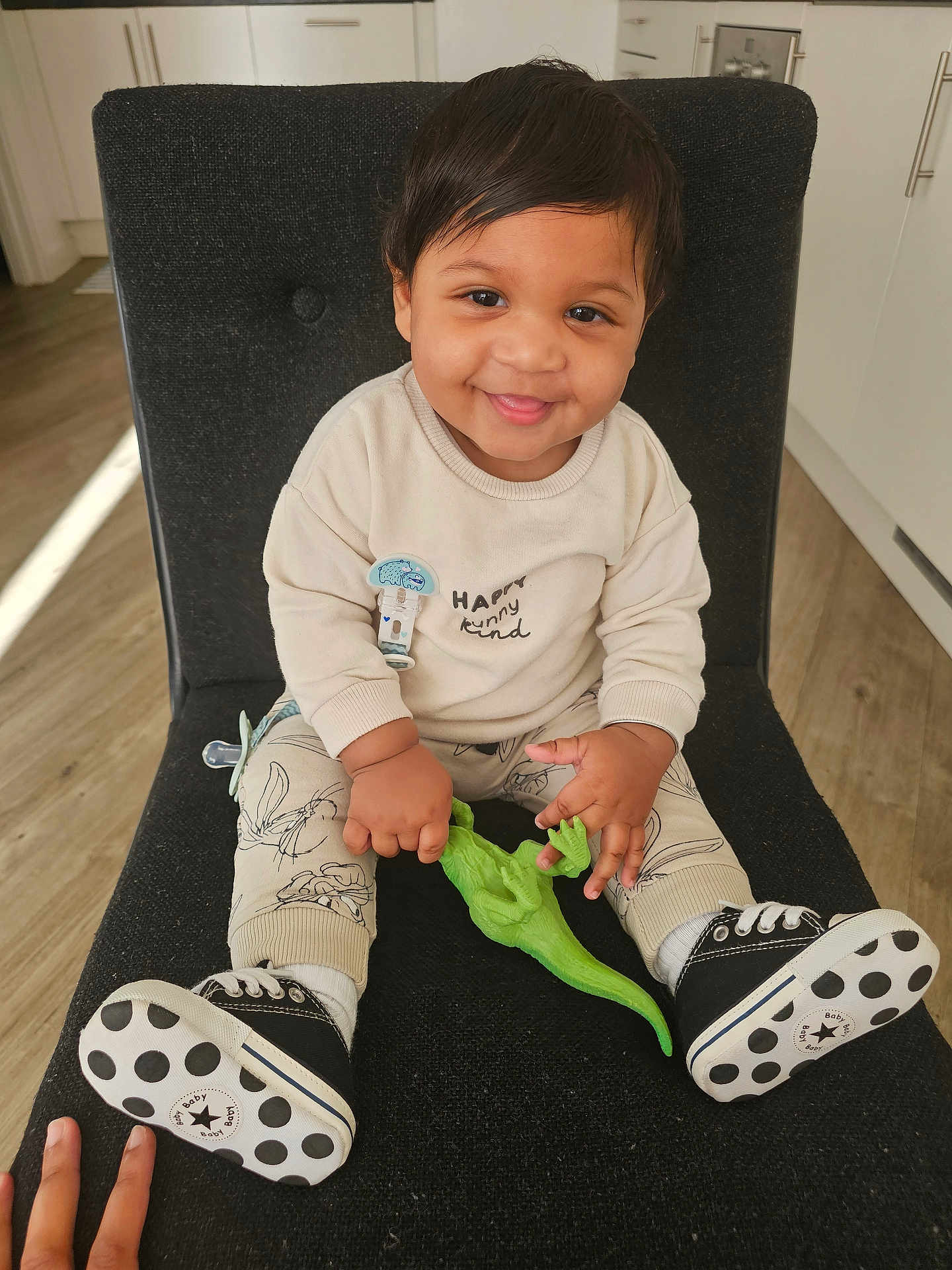 Syron is registered to the contest to win money with this photo: black_chair, cabinet, child, clothing, cute, dinosaur_toy, flooring, hand, happy, indoor, kitchen, pacifier_clip, person, polka_dots, portrait, sitting, smiling, sneakers, toddler, toy