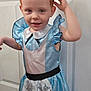 child, costume, alice_in_wonderland, blue_dress, headband, black_ears, smiling, portrait, indoor, door, playful, young_child, red_hair, curly_hair, white_collar, apron, floor, human, person, cute