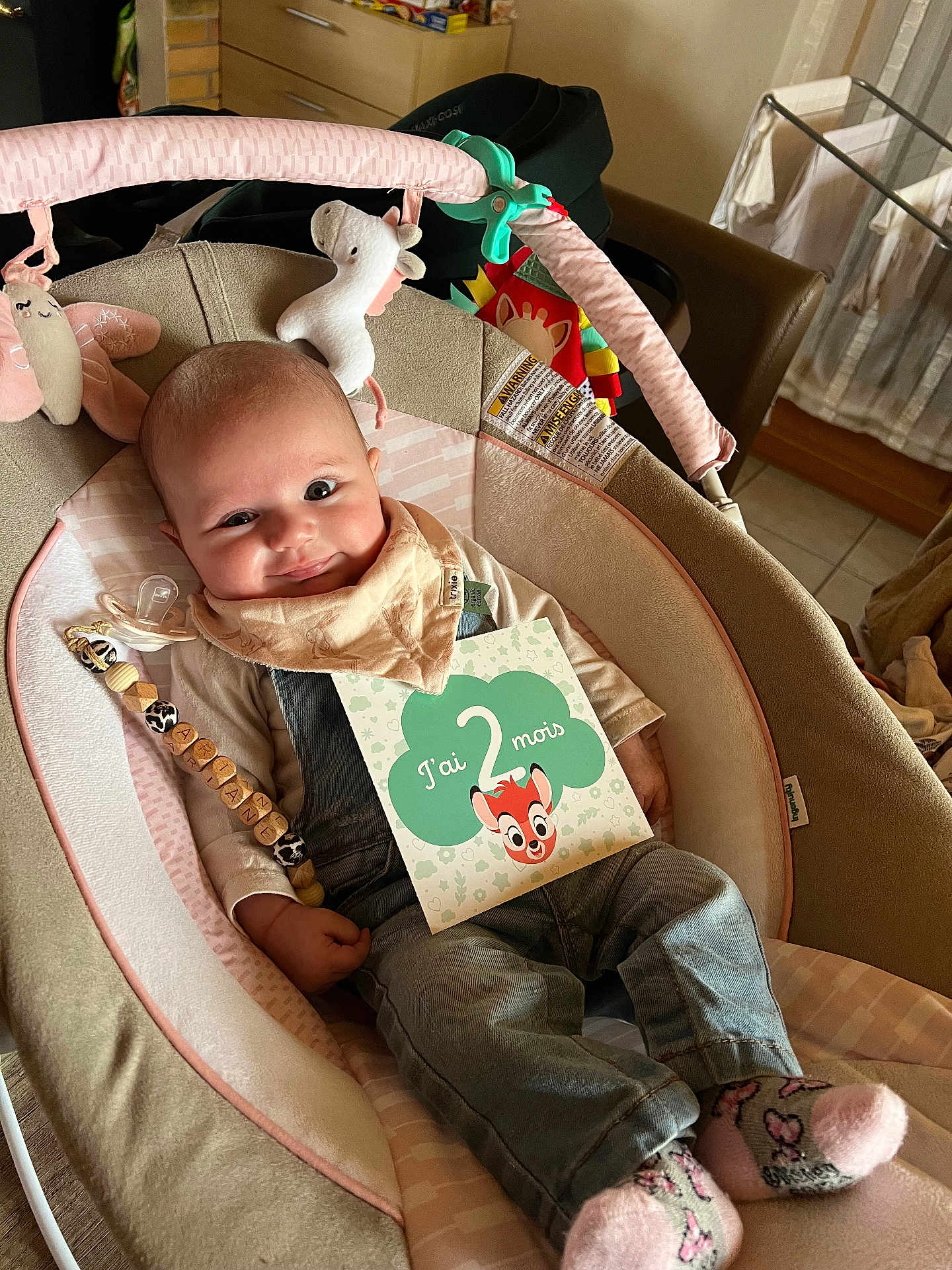 Ariane participe au concours pour gagner de l'argent avec cette photo : baby, baby_seat, bib, card, child, clothing, cozy, cute, denim_overalls, face, flooring, indoor, infant, pacifier, person, relaxing, smile, socks, soft_toys, toy