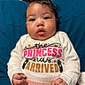 Zoey is registered to the contest to win money with this photo: baby, infant, child, onesie, clothing, sitting, blue_cushion, face, eyes, hands, cute, portrait, indoors, human, skin, pink_pants, text_on_clothing, white_onesie, expression, young