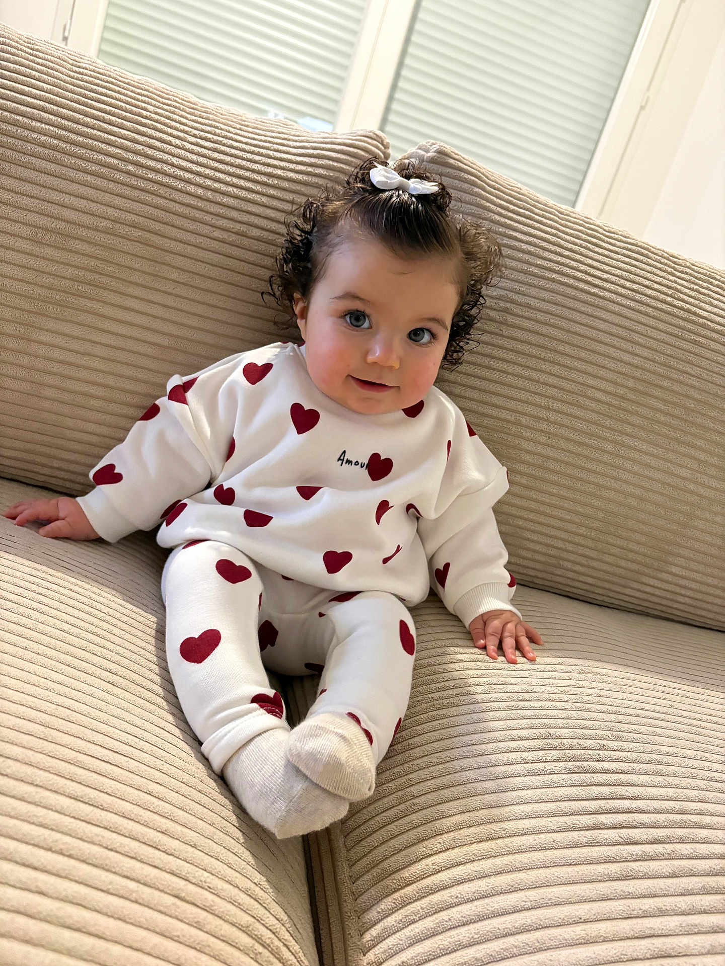 Romy participe au concours pour gagner de l'argent avec cette photo : child, baby, infant, couch, sofa, heart_pattern, sweater, leggings, bow, curly_hair, smile, blue_eyes, socks, indoors, portrait, soft_furniture, cozy, cute, window, playful