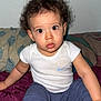 baby, blue_pants, casual_clothing, child, curly_hair, cute, expression, face, home, indoor, person, pillow, plush_blanket, portrait, sitting, skin, toddler, white_tshirt, wide_eyes, young_child