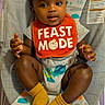 baby, child, bib, orange_bib, socks, yellow_socks, baby_seat, infant, cute, smiling, face, human, clothing, indoor, person, toddler, patterned_seat, feeding, happy, expression