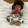 Dakota joined the competition — help win amazing prizes! baby, child, cowboy_costume, hat, bandana, pants, boots, bed, white_bedspread, indoor, portrait, cute, infant, sitting, clothing, costume, headwear, footwear, person, baby_fashion