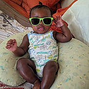Dakota joined the competition — help win amazing prizes! baby, sunglasses, pillow, bed, infant, child, cute, smiling, patterned_clothing, green_sunglasses, relaxing, indoor, person, one_person, toddler, comfortable, playful, skin, headwear, expression