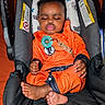 baby, infant, sleeping, car_seat, orange_clothing, pacifier, black_car_seat, indoors, child, cute, peaceful, relaxed, toddler, clothing, footwear_barefoot, head_support, seat_belt, baby_gear, portrait, resting