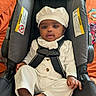 Dakota joined the competition — help win amazing prizes! baby, child, car_seat, white_outfit, hat, infant, sitting, indoors, curious, expression, skin, barefoot, seatbelt, orange_background, clothing, person, cute, portrait, young_child, comfortable