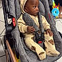 baby, child, stroller, gray_quilted, beige_outfit, bear_prints, toy, floor_tiles, indoor, seated, infant, hooded_jacket, footwear, hand, curious, person, shopping_cart, safety_strap, doll, colorful