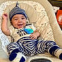 baby, infant, smiling, striped_clothing, hat, teething_toy, baby_seat, cushion, bear_pattern, happy, child, cute, indoor, person, footwear, sock, relaxed, portrait, playful, young