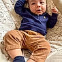 baby, infant, child, baby_seat, bear_pattern, navy_sweater, corduroy_pants, navy_socks, striped_socks, face, smile, cute, indoor, cozy, clothing, furniture, relaxing, portrait, person, comfort