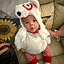 baby, child, costume, polar_bear, cute, striped_pants, red_and_white, couch, pillow, sunflower, indoor, person, soft_toys, warm_clothing, socks, hand, expression, seated, plush, cozy