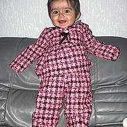Katalëya participe au concours pour gagner de l'argent avec cette photo : apparel, baby, checkered_clothing, child, cute, face, feet, hair, happy, home, indoor, leather_couch, person, pink_outfit, portrait, smiling, standing, texture, toddler, wall