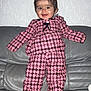 apparel, baby, checkered_clothing, child, cute, face, feet, hair, happy, home, indoor, leather_couch, person, pink_outfit, portrait, smiling, standing, texture, toddler, wall
