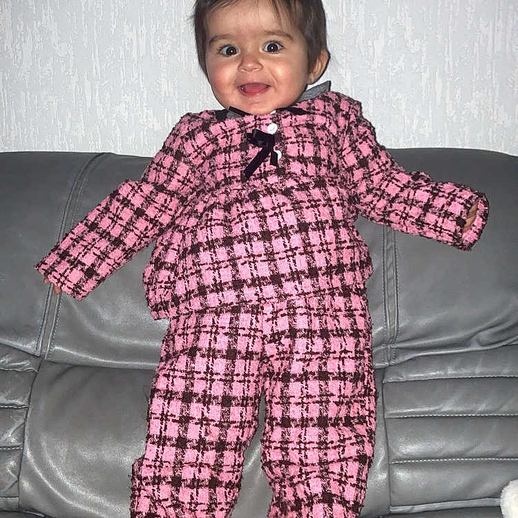 Katalëya participe au concours pour gagner de l'argent avec cette photo : apparel, baby, checkered_clothing, child, cute, face, feet, hair, happy, home, indoor, leather_couch, person, pink_outfit, portrait, smiling, standing, texture, toddler, wall