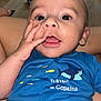 Eden participe au concours pour gagner de l'argent avec cette photo : baby, infant, child, face, hand, blue_shirt, fish_print, text, eyes, mouth, tongue, skin, person, clothing, sitting, indoors, table, background, expression, cute