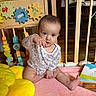 Taylynn is registered to the contest to win money with this photo: baby, infant, playpen, toy, plush, yellow, pink_blanket, wooden_bars, curious, sitting, indoors, child, face, hand, floor, clothing, head, expression, room, book