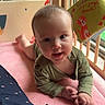 Taylynn is registered to the contest to win money with this photo: baby, infant, crib, toy, pink_blanket, green_clothing, face, hand, window, natural_light, hanging_toys, smiling, child, indoor, playful, curious, crawling, person, soft_texture, cute