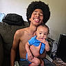 teenager, baby, afro, smiling, blue_clothing, couch, indoor, family, child, holding, happy, person, casual, home, furniture, sitting, expression, portrait, candid, relaxed