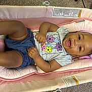Leilani is registered to the contest to win money with this photo: baby, infant, smiling, headband, flower, pink, cushion, seat, clothing, shorts, happy, playful, indoor, carpet, skin, person, child, cute, young, portrait