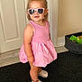 toddler, child, pink_dress, sunglasses, red_bow, white_crocs, anklet, indoor, door, rug, floor, toy_basket, playroom, fashion, cute, portrait, standing, person, smiling, accessories