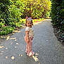 child, toddler, girl, standing, path, outdoor, sunlight, greenery, plants, shoes, bow, pink_pants, cream_top, nature, smile, portrait, daylight, casual_clothing, side_view, happy