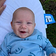 Noah is registered to the contest to win money with this photo: baby, smile, blue_clothing, infant, outdoor, grass, cushion, hand, happy, face, person, young_child, lying_down, closeup, skin, head, cheerful, baby_clothes, child, nature