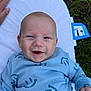 baby, smile, blue_clothing, infant, outdoor, grass, cushion, hand, happy, face, person, young_child, lying_down, closeup, skin, head, cheerful, baby_clothes, child, nature