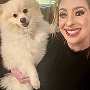Millie is registered to the contest to win money with this photo: woman, dog, indoor, smiling, fluffy_dog, white_dog, black_clothing, holding, pet, happy, portrait, window, blinds, face, long_hair, tongue_out, cute, domestic_animal, human_animal_interaction, casual