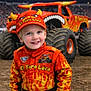 Owen is registered to the contest to win money with this photo: child, smiling, orange_clothing, cap, monster_truck, flames, race_suit, outdoor, event, dirt, vehicle, toy, portrait, happy, young, boy, crowd, stadium, blue_eyes, short_hair
