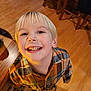 Owen is registered to the contest to win money with this photo: child, blond_hair, smile, plaid_shirt, indoor, wooden_floor, table, chair, happy, person, teeth, face, casual_clothing, cute, playful, young, childhood, portrait, light, home