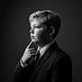 child, boy, portrait, black_and_white, suit, tie, thinking, pose, profile, studio, lighting, formal, young, expression, face, hair, clothing, monochrome, serious, background