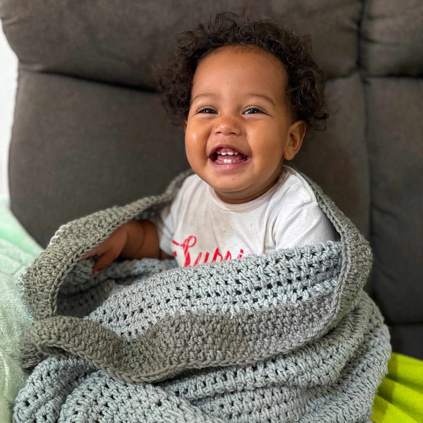 Leeroy a rejoint le concours — aidez-le/la à gagner de superbes lots ! toddler, child, smiling, blanket, knitted_blanket, couch, indoor, happy, cute, person, curly_hair, white_tshirt, portrait, seated, cozy, homedecor, warm, comfort, baby, expression