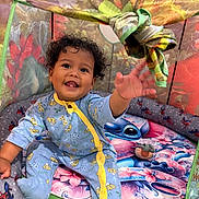 Leeroy participe au concours pour gagner de l'argent avec cette photo : baby, child, curly_hair, smiling, playpen, colorful, pajamas, blue, yellow, toy, indoor, cute, happy, reaching_hand, patterned, fabric, floor, cushion, person, infant