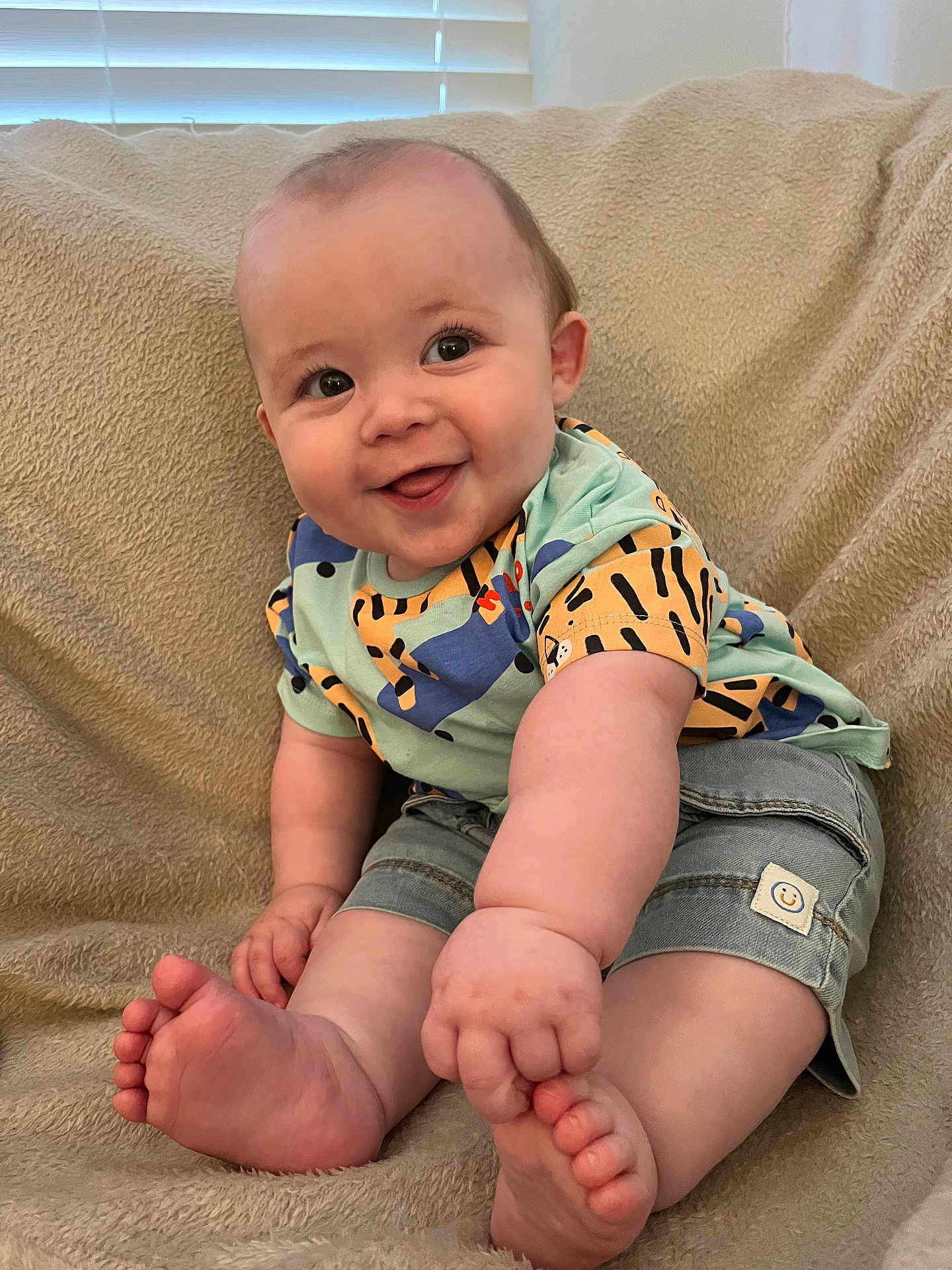 Jackson joined the competition — help win amazing prizes! baby, smiling, tongue_out, sitting, denim_shorts, colorful_shirt, cozy_blanket, barefoot, cute, happy, infant, child, indoors, plush, face, legs, feet, chubby, portrait, playful