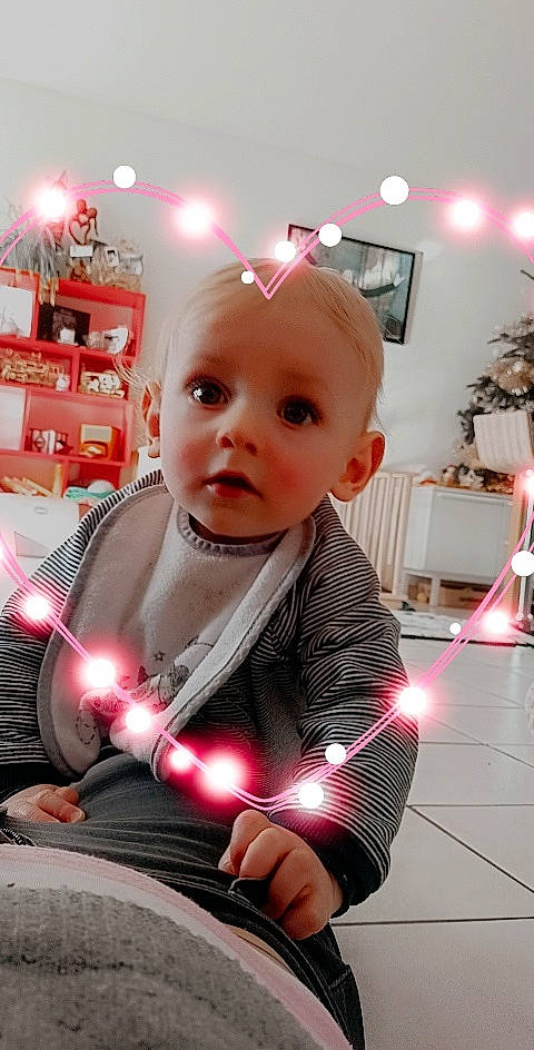 Evann a rejoint le concours — aidez-le/la à gagner de superbes lots ! baby, baby_toddler_clothing, blond, cheek, child, child_model, curious, home, houseplant, interior_design, lamp, light_fixture, lighting, lighting_accessory, living_room, person, picture_frame, pink, sitting, surprise