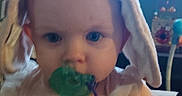 Haisley is registered to the contest to win money with this photo: baby, blue_eyes, child, close_up, cute, dress, frilly_outfit, furniture, green_pacifier, home, hood, indoor, infant, pacifier, photography, portrait, sitting, smiling, white_clothing, window