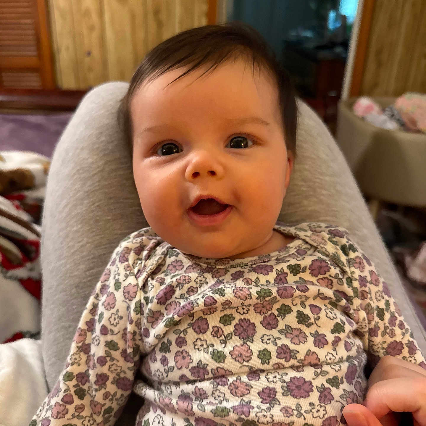 Charlotte joined the competition — help win amazing prizes! baby, child, smiling, face, person, indoor, clothing, floral_pattern, onesie, hand, lap, wood_paneling, furniture, cushion, happy, portrait, infant, skin, hair, cozy