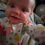 Sara joined the competition — help win amazing prizes! baby, child, onesie, fruit_pattern, face, expression, wide_eyes, blurry, close_up, indoor, blanket, fan, clothing, person, home, curious, cute, infant, portrait, soft