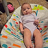 baby, infant, child, portrait, indoors, bouncer, baby_seat, lying_down, sitting, wide_eyed, calm, clothing, onesie, barefoot, feet, toy, pink_toy, carpet, colorful, home