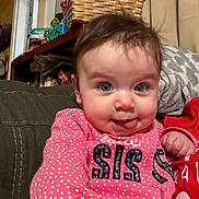 Arya is registered to the contest to win money with this photo: baby, child, face, tongue_out, blue_eyes, pink_clothing, polka_dot, cute, indoor, living_room, basket, expression, person, portrait, smiling, sitting, hair, hand, cozy, home