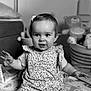 baby, child, infant, sitting, play_mat, toys, basket, flower_pattern, hair_clip, black_and_white, portrait, smiling, cute, indoor, person, happy, face, clothing, expression, young