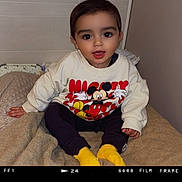 Isaac participe au concours pour gagner de l'argent avec cette photo : child, toddler, sitting, mickey_mouse, sweatshirt, yellow_socks, blanket, indoors, cute, smiling, face, person, clothing, portrait, young_child, happy, cozy, soft_texture, casual, baby