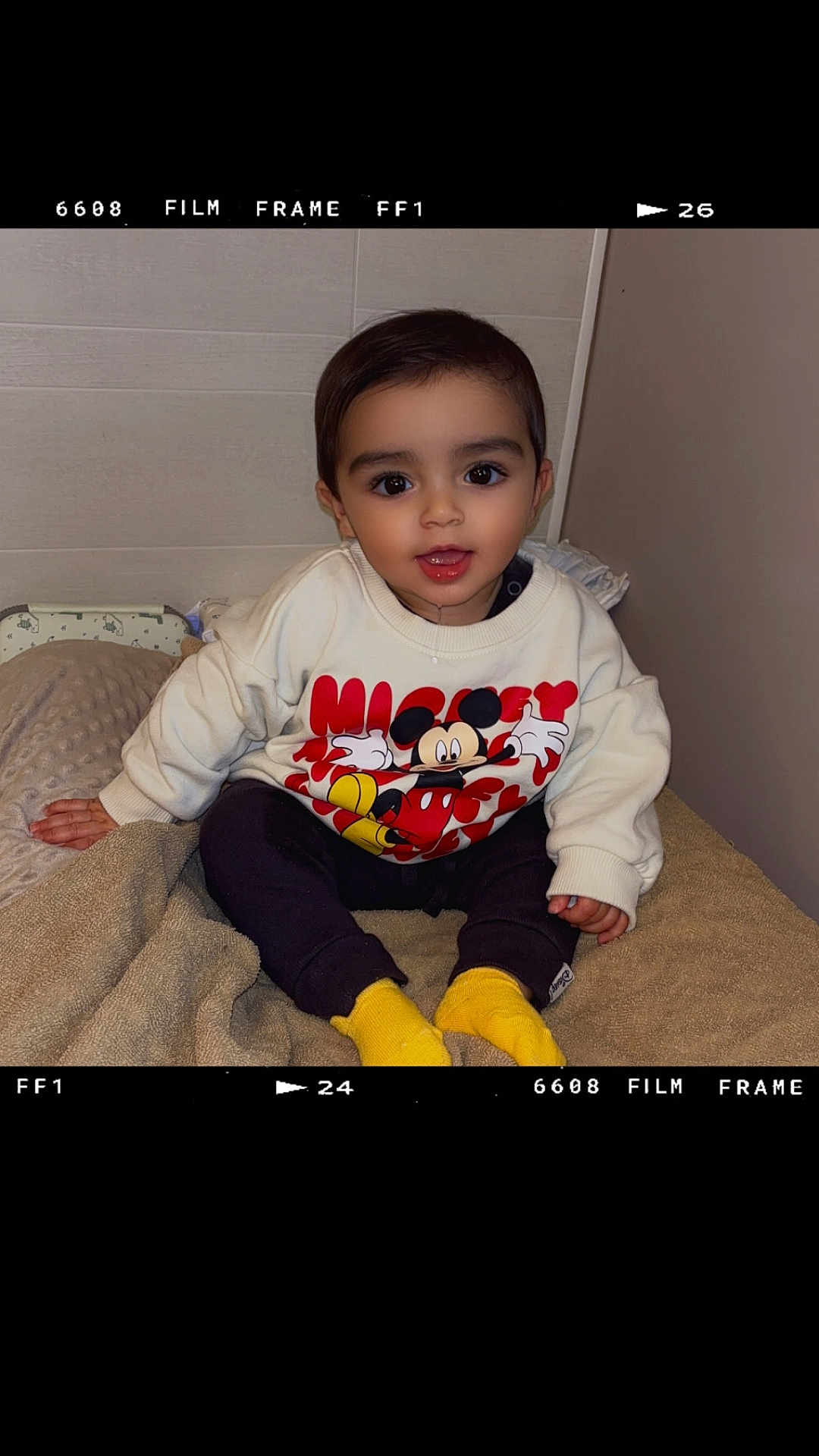 Isaac participe au concours pour gagner de l'argent avec cette photo : child, toddler, sitting, mickey_mouse, sweatshirt, yellow_socks, blanket, indoors, cute, smiling, face, person, clothing, portrait, young_child, happy, cozy, soft_texture, casual, baby