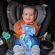 Samson joined the competition — help win amazing prizes! baby, car_seat, child, blue_eyes, orange_sweater, blanket, gray_booties, smiling, indoor, seatbelt, toy, car_interior, cute, infant, happy, clothing, portrait, holding, cozy, comfort