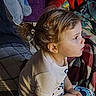 child, toddler, portrait, profile, face, hair, ponytail, eyes, ear, nose, mouth, clothing, shirt, blanket, couch, indoor, home, seated, curious, colorful