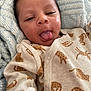 baby, infant, face, tongue, onesie, clothing, pattern, knitted_blanket, cozy, cute, skin, head, person, sleepwear, newborn, indoor, expression, portrait, child, lying_down