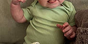 Aspen is registered to the contest to win money with this photo: baby, child, tongue_out, green_onesie, blanket, couch, soft_texture, face, hand, infant, cute, indoor, portrait, skin, expression, sitting, young_child, comfort, cozy, furniture